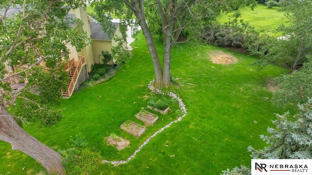 view of grassy yard featuring a wooden deck, stairway, and a garden