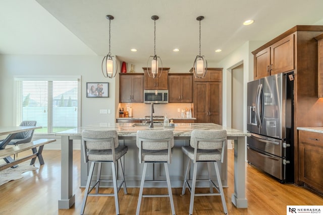 6707 S 209th St, Omaha, NE 68022 - kitchen featuring stainless steel appliances, light wood-style floors, decorative backsplash, a center island with sink, and light stone counters