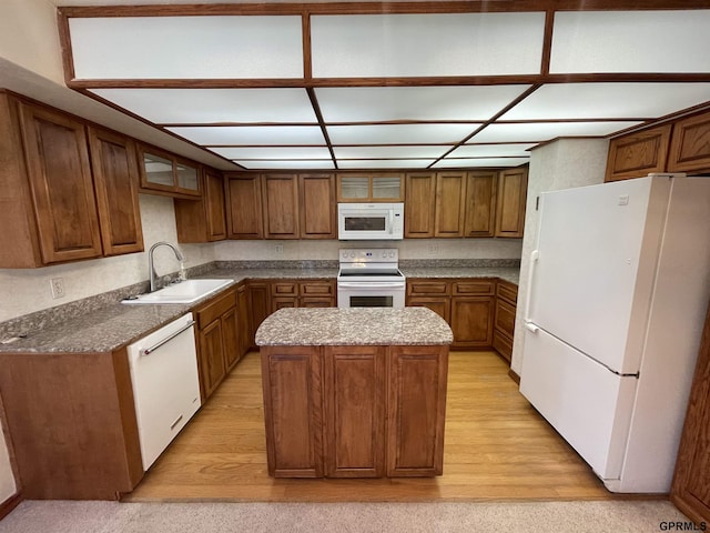kitchen with white appliances, a sink, a center island, light wood-style floors, and glass insert cabinets
