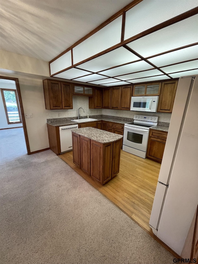 kitchen featuring white appliances, a sink, a center island, and light carpet