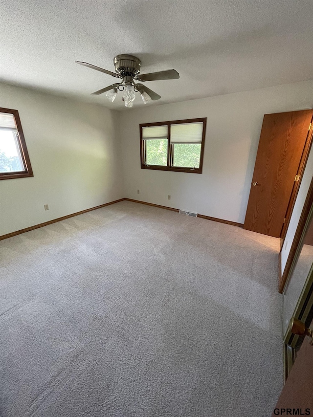 empty room with healthy amount of natural light, carpet flooring, baseboards, a textured ceiling, and a ceiling fan