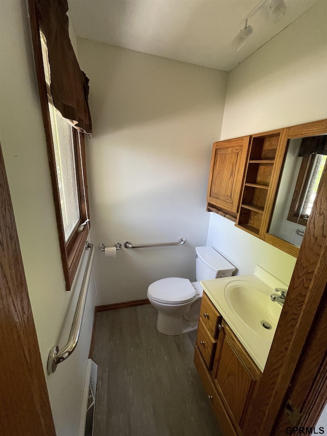 bathroom with wood finished floors, toilet, vanity, radiator, and baseboards
