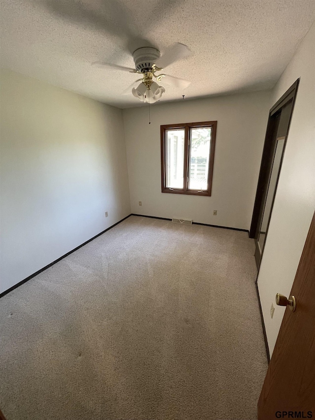 spare room featuring light carpet, a ceiling fan, baseboards, and a textured ceiling