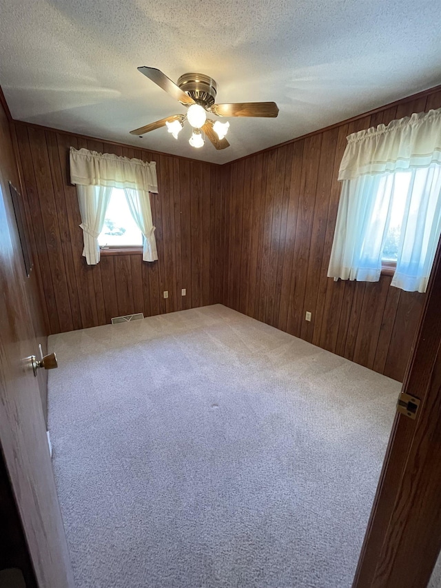 unfurnished room with carpet floors, a textured ceiling, a ceiling fan, and wooden walls