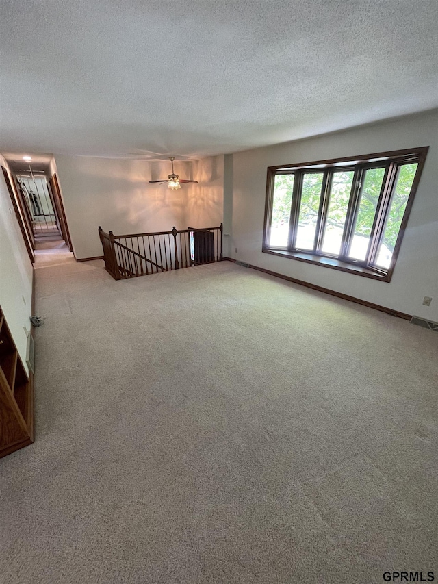 carpeted empty room with a textured ceiling, baseboards, and a ceiling fan