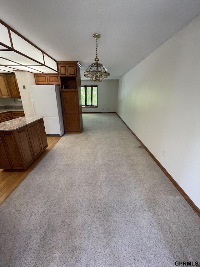 unfurnished living room with a chandelier, light colored carpet, and baseboards