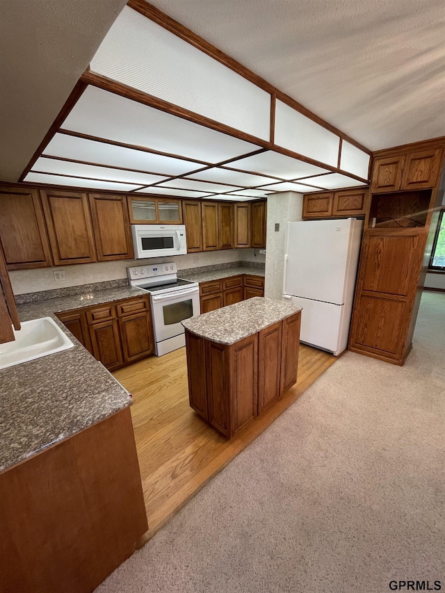 kitchen featuring white appliances, brown cabinetry, a kitchen island, and a sink