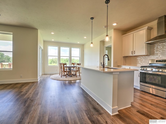 kitchen with wall chimney exhaust hood, stainless steel gas stove, a sink, dark wood-style flooring, and white cabinetry