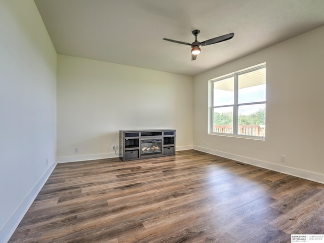 empty room with ceiling fan, a glass covered fireplace, wood finished floors, and baseboards