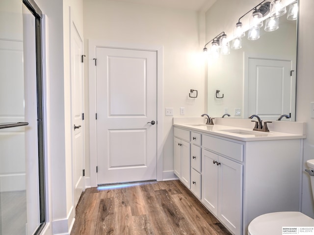 bathroom with toilet, wood finished floors, double vanity, and a shower with shower door