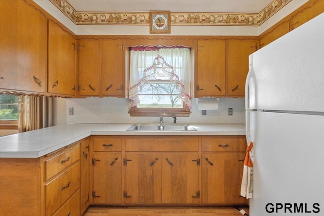 kitchen featuring freestanding refrigerator, a sink, light countertops, a peninsula, and brown cabinets