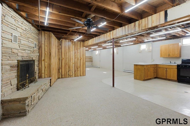 basement with a baseboard radiator, a sink, a fireplace, a ceiling fan, and light carpet