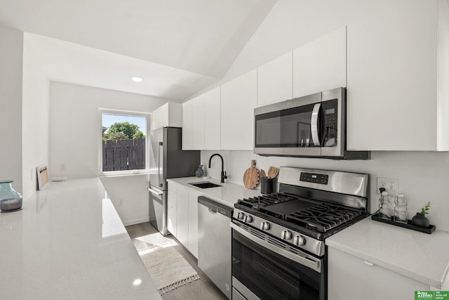 kitchen featuring appliances with stainless steel finishes, a sink, lofted ceiling, white cabinets, and light countertops
