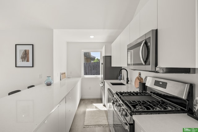 kitchen with appliances with stainless steel finishes, a sink, white cabinets, light countertops, and light wood-type flooring