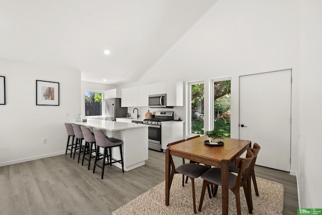 dining room with light wood-style flooring, high vaulted ceiling, recessed lighting, and baseboards
