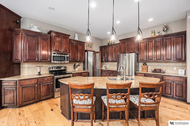 2705 N 189th St, Omaha, NE 68022 - kitchen with appliances with stainless steel finishes, a sink, decorative backsplash, a center island with sink, and light wood-style floors