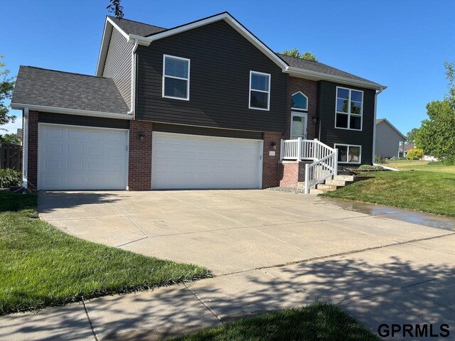 2110 Herel St, Lincoln, NE 68512 - bi-level home with brick siding, driveway, a front lawn, a garage, and roof with shingles