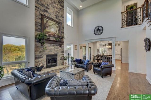 living area with decorative columns, a towering ceiling, light wood finished floors, baseboards, and a fireplace