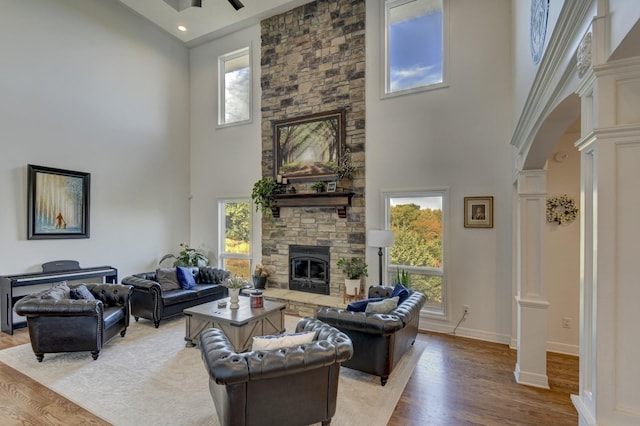 living area featuring ornate columns, a high ceiling, plenty of natural light, a fireplace, and light wood-style flooring