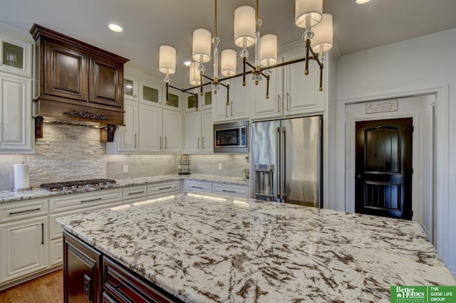 kitchen featuring stainless steel appliances, glass insert cabinets, a chandelier, backsplash, and light stone counters