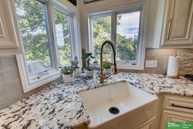 kitchen view of a sink, decorative backsplash, and light stone counters
