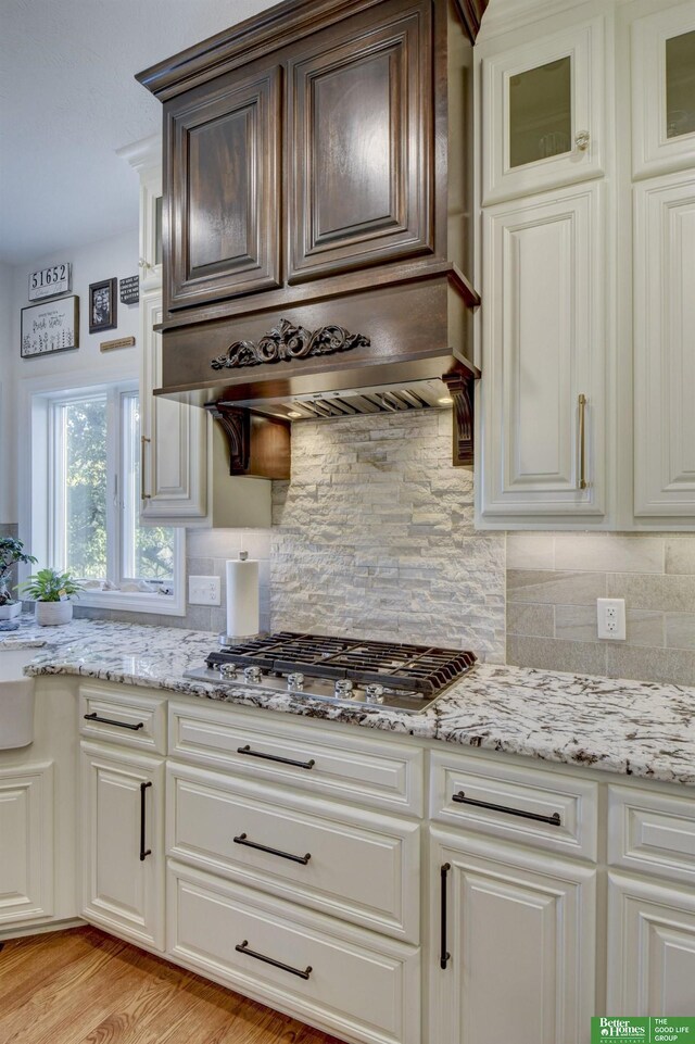 kitchen with light stone counters, backsplash, stainless steel gas stovetop, and white cabinetry