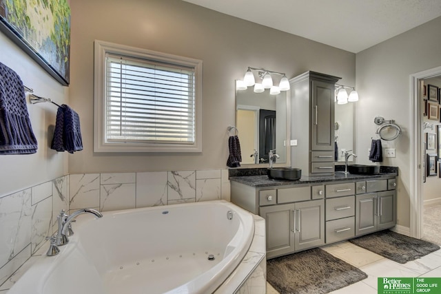 bathroom with a tub with jets, double vanity, and baseboards