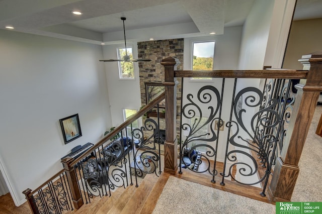 stairs with a raised ceiling, wood finished floors, and recessed lighting