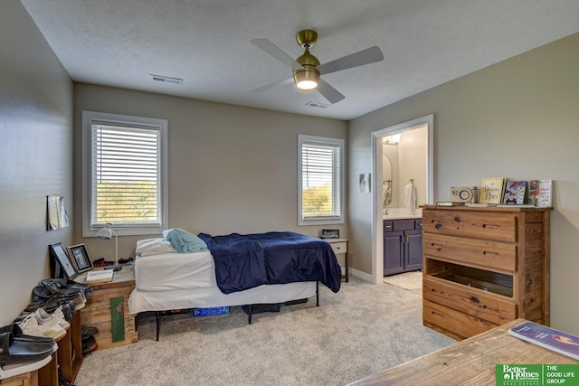 bedroom with light colored carpet, ensuite bathroom, ceiling fan, a textured ceiling, and baseboards
