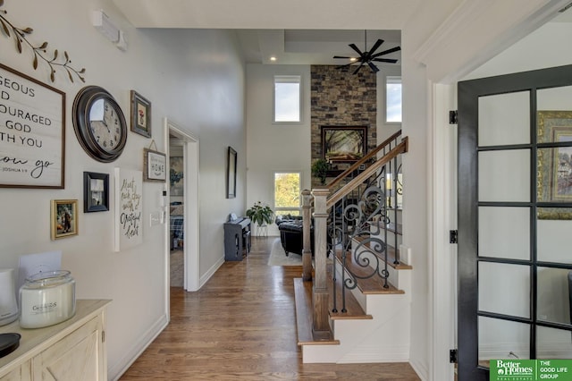 entryway with plenty of natural light, stairs, wood finished floors, ceiling fan, and a towering ceiling