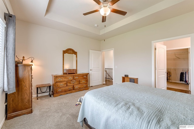 bedroom featuring carpet flooring, baseboards, a tray ceiling, a spacious closet, and a ceiling fan
