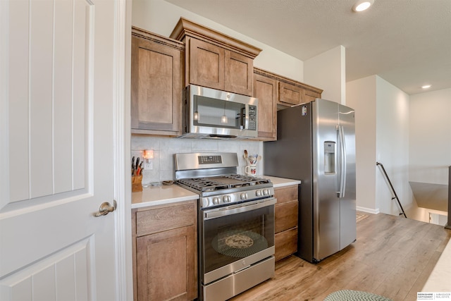 kitchen with appliances with stainless steel finishes, light wood finished floors, light countertops, brown cabinetry, and backsplash