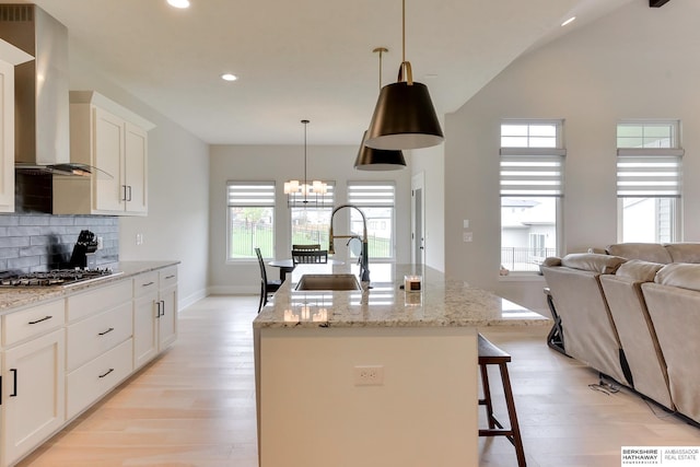 18108 Locust St, Elkhorn, NE 68022 - kitchen featuring a sink, wall chimney range hood, stainless steel gas cooktop, light wood-type flooring, and an island with sink
