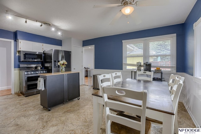 dining area featuring ceiling fan and a wainscoted wall