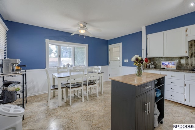 kitchen featuring ceiling fan, a wainscoted wall, white cabinets, decorative backsplash, and wood counters