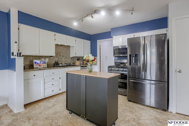 kitchen featuring appliances with stainless steel finishes, a sink, white cabinets, backsplash, and a kitchen island