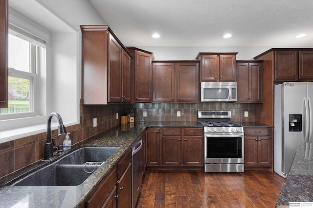 18652 Van Camp Dr, Omaha, NE 68130 - kitchen featuring appliances with stainless steel finishes, a sink, dark wood-type flooring, dark stone countertops, and tasteful backsplash