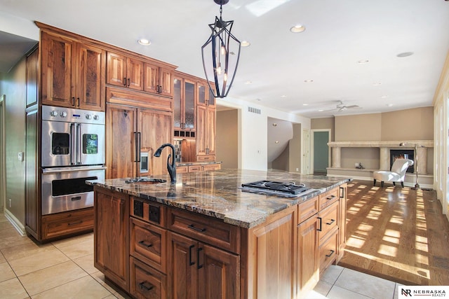 1125 Stone Creek Dr, Blair, NE 68008 - kitchen featuring stainless steel appliances, a sink, light tile patterned floors, a center island with sink, and glass insert cabinets