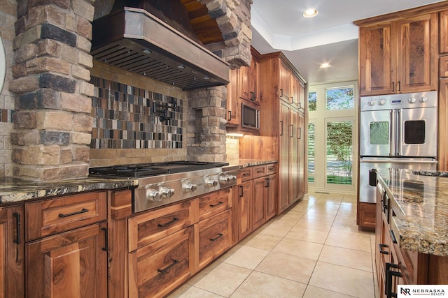 1125 Stone Creek Dr, Blair, NE 68008 - kitchen with ventilation hood, appliances with stainless steel finishes, backsplash, dark stone countertops, and light tile patterned flooring