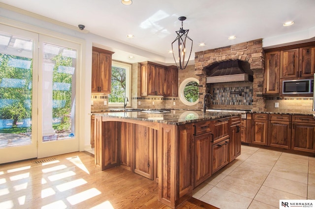 1125 Stone Creek Dr, Blair, NE 68008 - kitchen with stainless steel microwave, a sink, dark stone counters, an island with sink, and tasteful backsplash