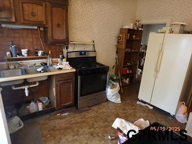 1935 S 11th St, Omaha, NE 68106 - kitchen with stainless steel range with gas stovetop, freestanding refrigerator, a sink, light countertops, and wallpapered walls