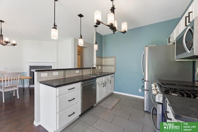 kitchen with appliances with stainless steel finishes, a chandelier, dark countertops, a sink, and white cabinetry