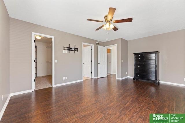unfurnished bedroom with wood finished floors, baseboards, a ceiling fan, and a walk in closet