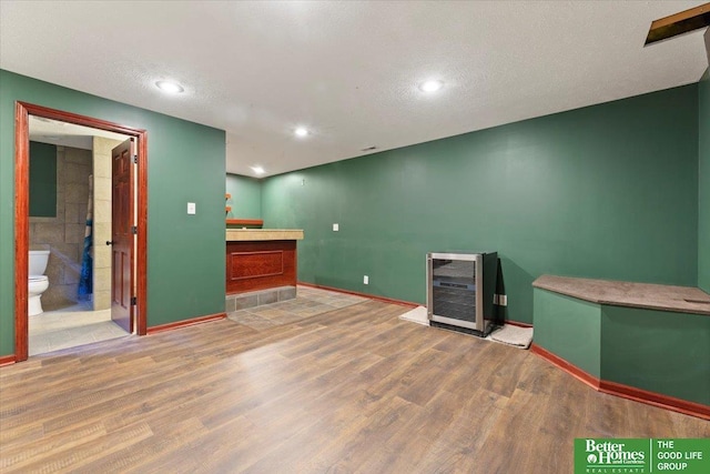 basement featuring wood finished floors, baseboards, beverage cooler, a textured ceiling, and recessed lighting