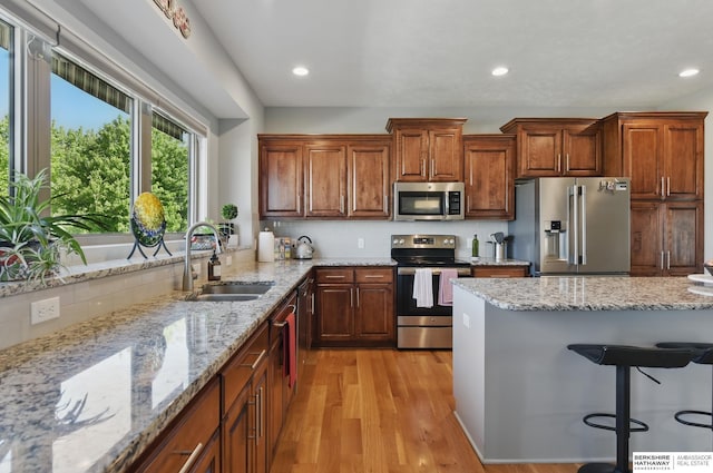 2614 N 191st Ave, Omaha, NE 68022 - kitchen with appliances with stainless steel finishes, a sink, light wood-type flooring, a breakfast bar, and light stone countertops