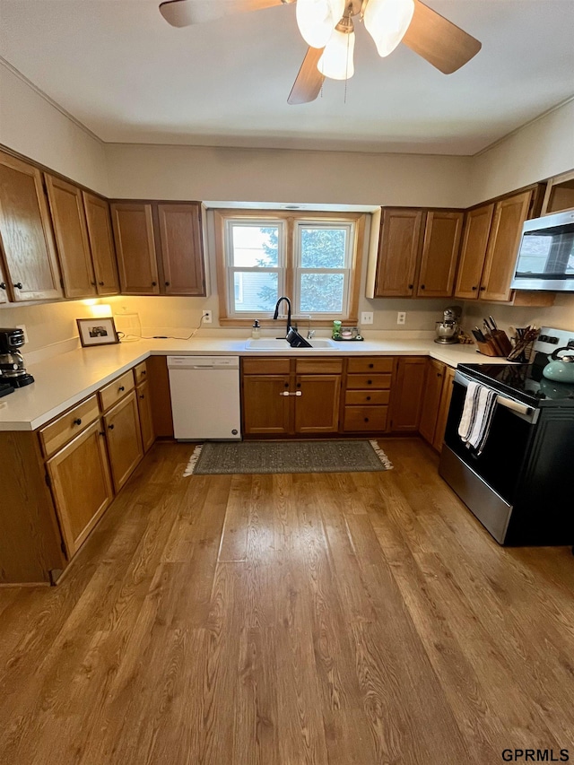 kitchen with appliances with stainless steel finishes, a sink, a ceiling fan, wood finished floors, and light countertops