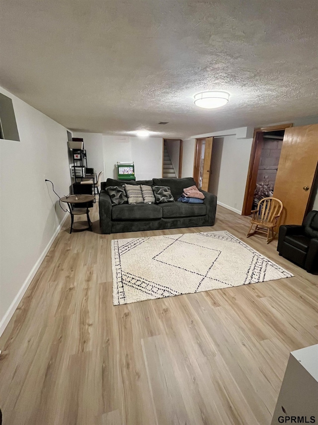 living room with light wood-style flooring, stairs, a textured ceiling, and baseboards
