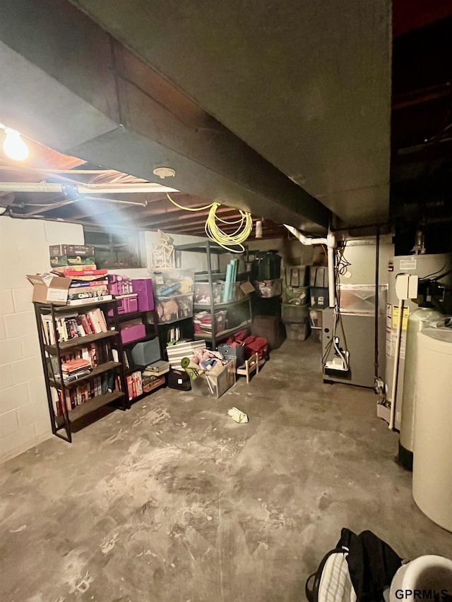 unfinished below grade area featuring water heater, heating unit, and concrete block wall