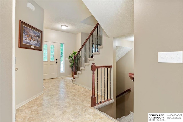 foyer with baseboards, a textured ceiling, and stairway