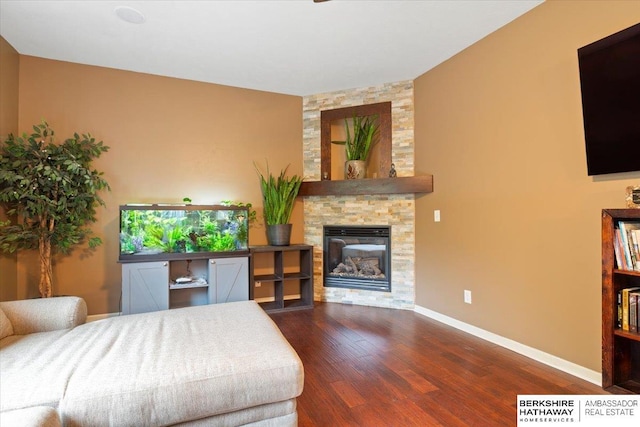 bedroom with dark wood finished floors, a stone fireplace, and baseboards